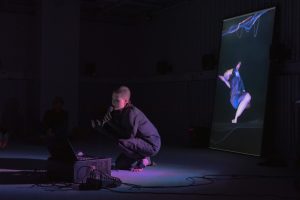 a person speaking to a microphone, behind is a screen that has a body image.